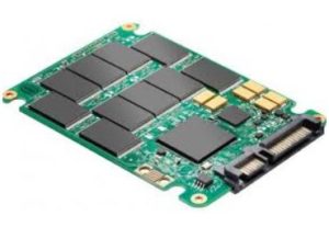 A bare solid-state drive with its circuit board and flash memory chips exposed, the SATA connector along one edge.