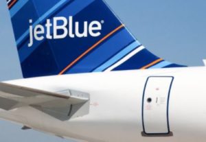 The tail and rear fuselage of a JetBlue aircraft on the tarmac, showing the blue tailfin and the jetBlue wordmark.