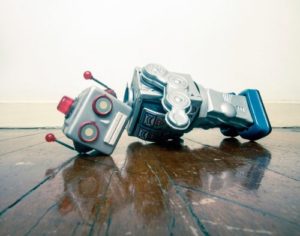 Two toy robots lying toppled on their sides on a wet, reflective wooden floor.